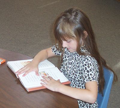 A girl sitting at a table reading a book