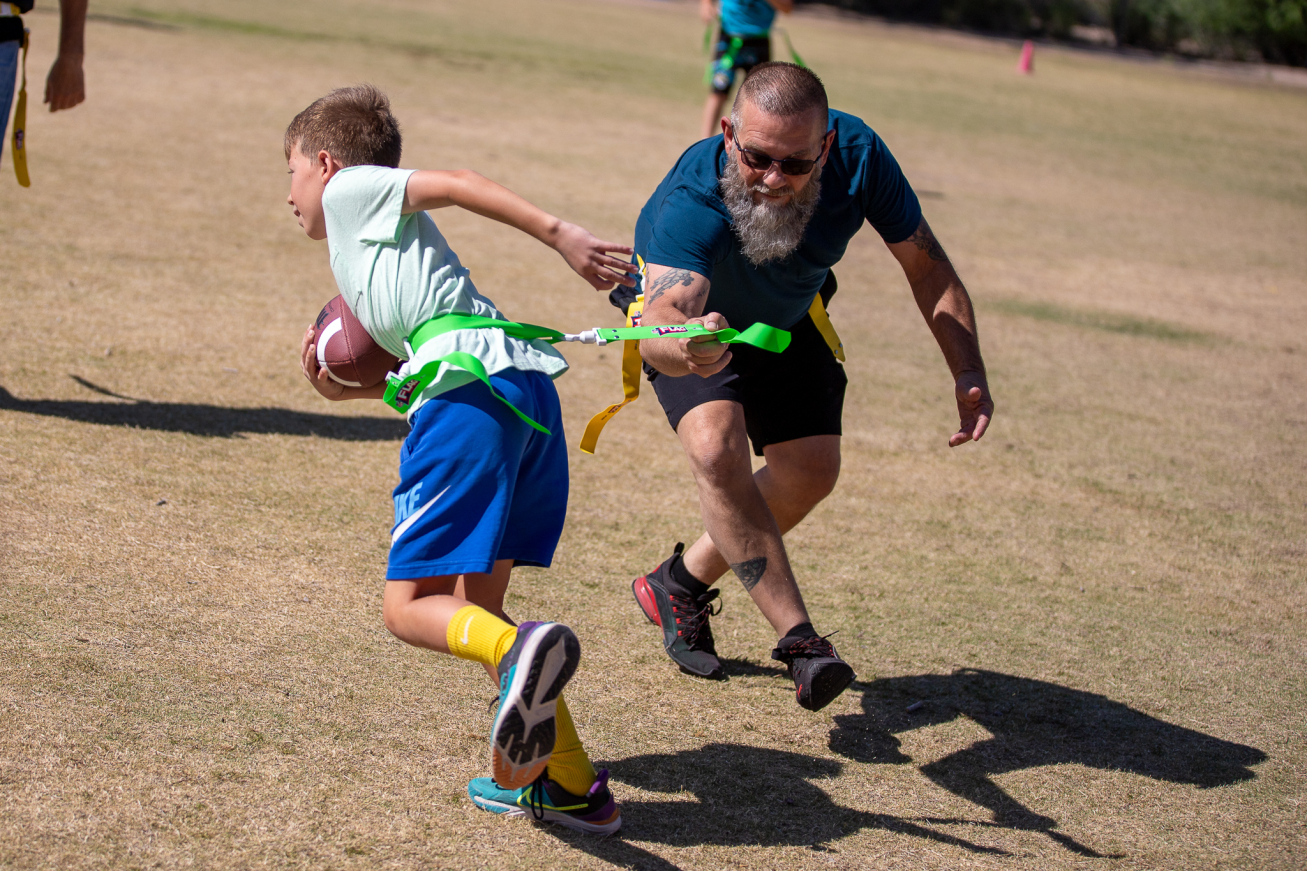 A boy runs with a football in his arms while a parent tries to grab his flag