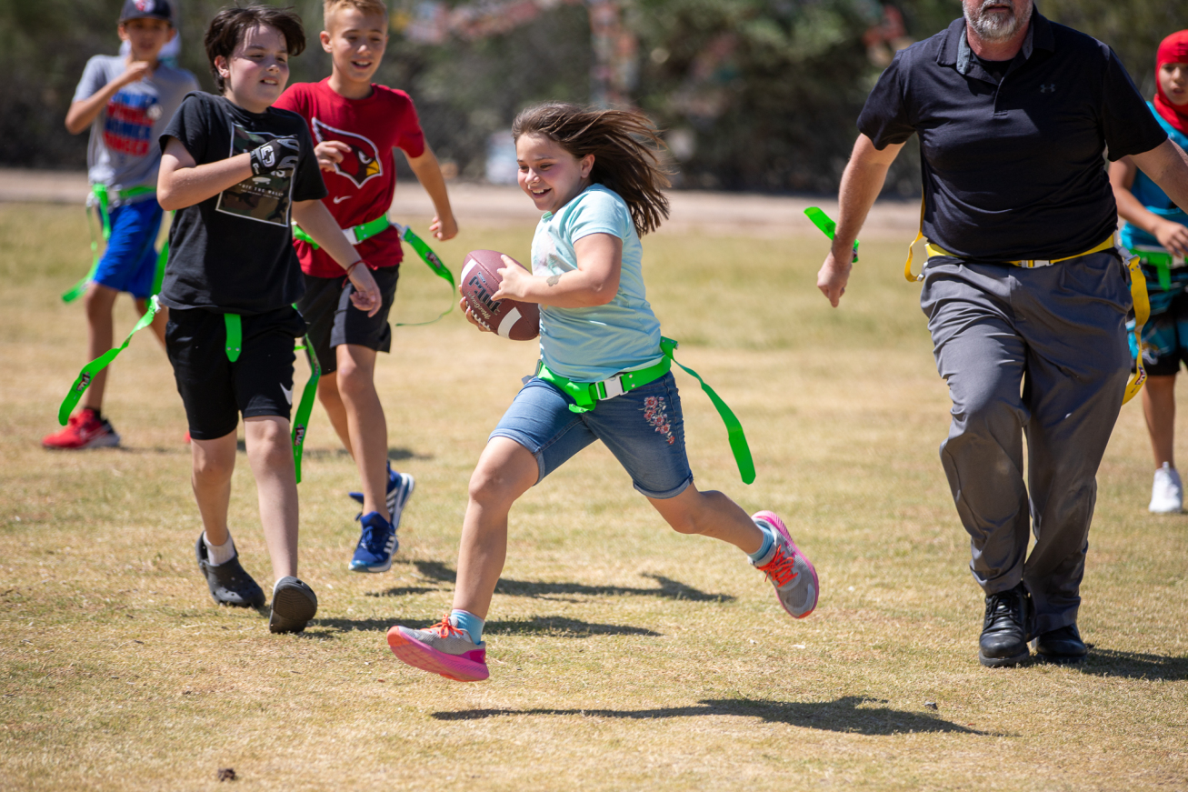 A girl smiles as she runs across the field with a football in her arms