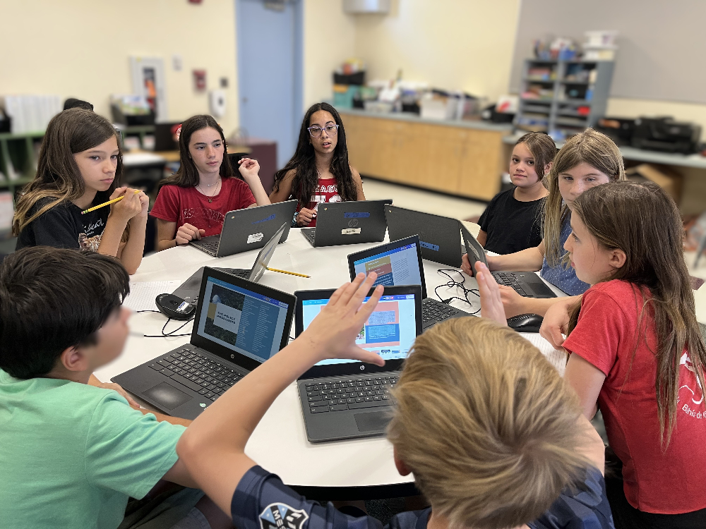 Students sit around a table with their laptops