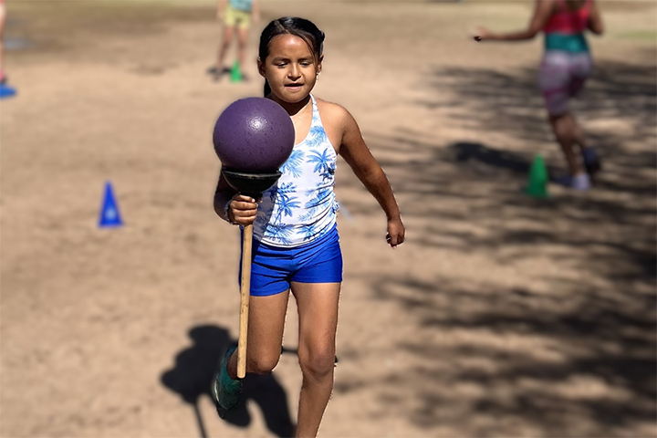 A girl runs across the field holding a purple ball on a plunger
