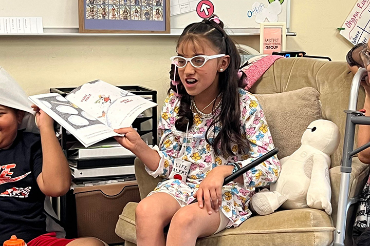 A girl dressed as an old lady reads a story to her classmates