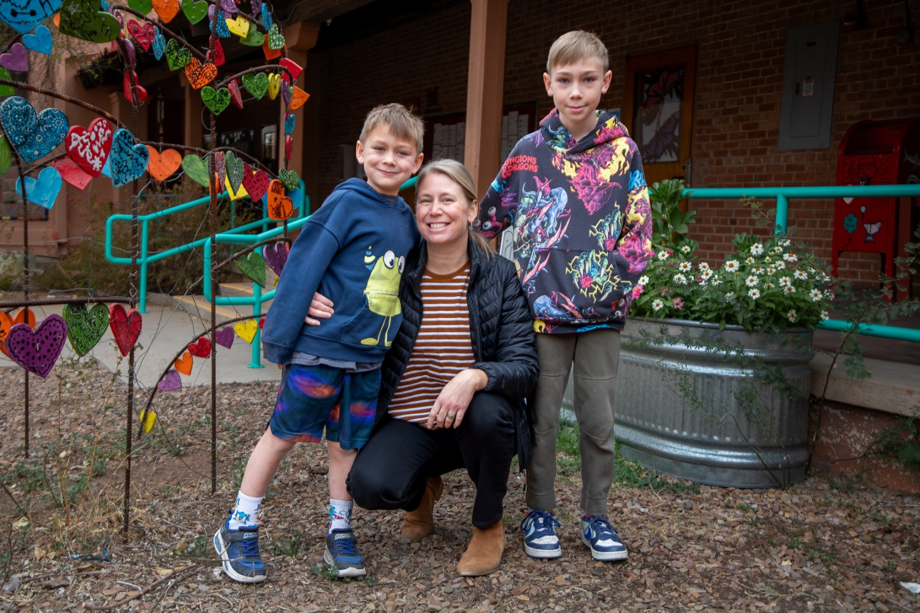 A woman with blonde hair poses with her two young sons in the school courtyard