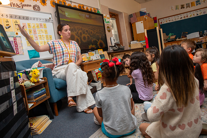 A woman points to a whiteboard to show her students something