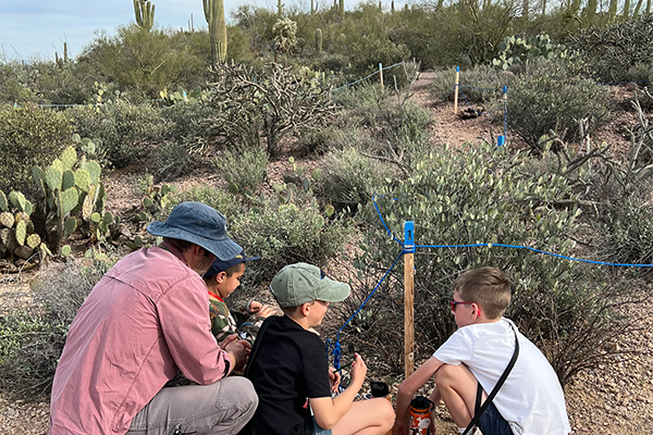 A man and three students kneel down to look at some plants