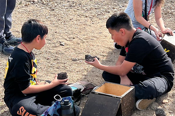 Two boys sitting on the ground look at rocks