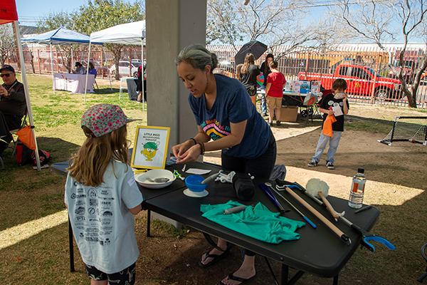 A woman standing behind a table shows a girl the tools she uses as an occupational therapist