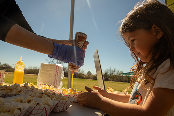 A woman squirts caramel sauce on a girl's bowl of popcorn