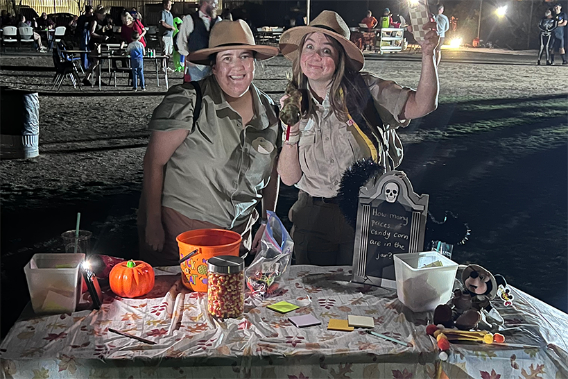 Two women dressed as explorers smile behind a table