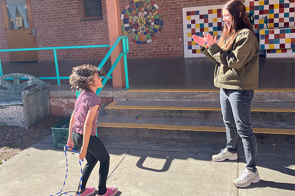 A woman claps for a little girl jumping rope