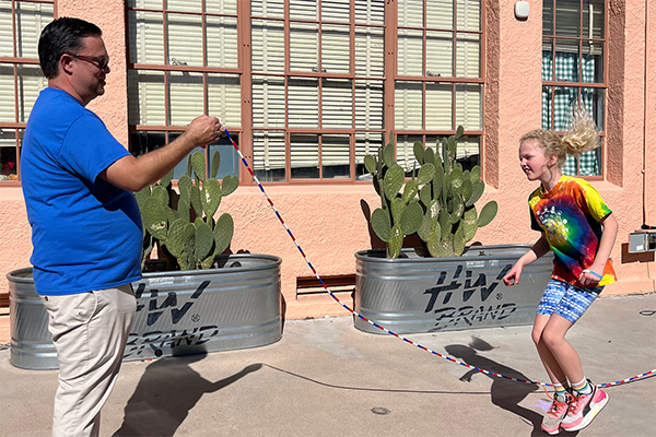 A man holds a rope for a girl to jump over