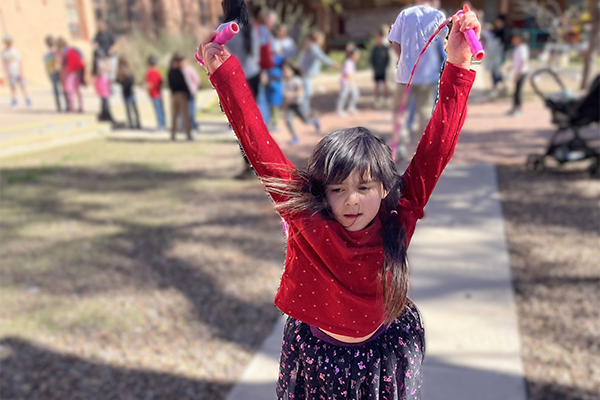 A little girl in a red shirt jumps rope