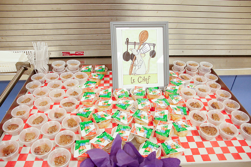 A table filled with small cups of snacks, and a picture of a rat in a chefs hat reading La Chef
