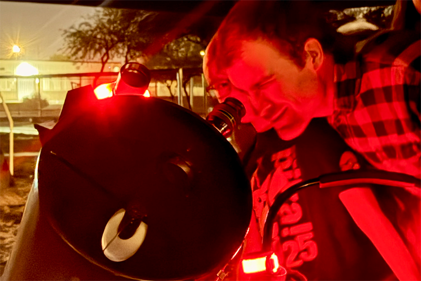 Students look into a telescope with a red light