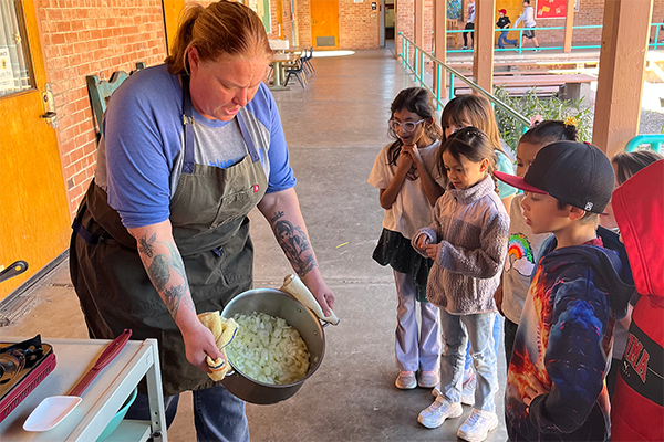 A woman holds a pot of rajas con crema for students to see