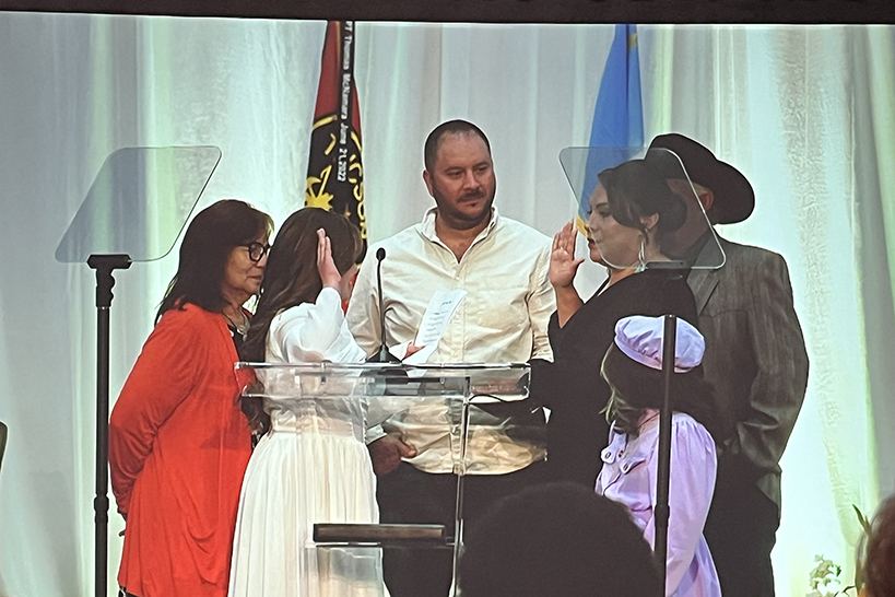 A group of people stand around a podium as a woman gets sworn into office