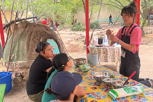 A woman excitedly shows students how to make pizza in the outdoor oven