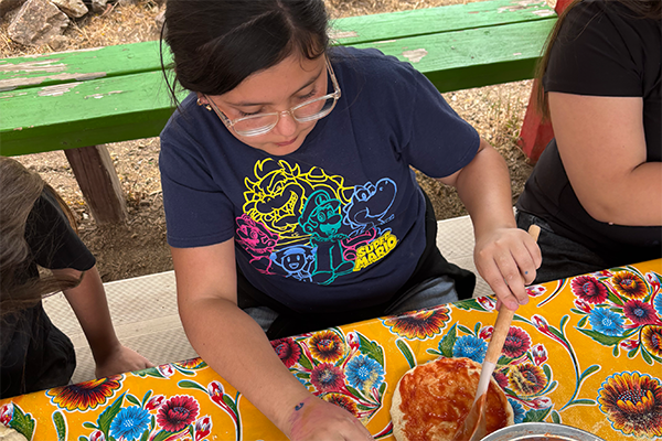 A girl spreads sauce on her pizza crust