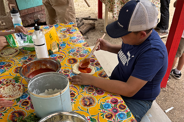 A boy spreads sauce on his pizza crust