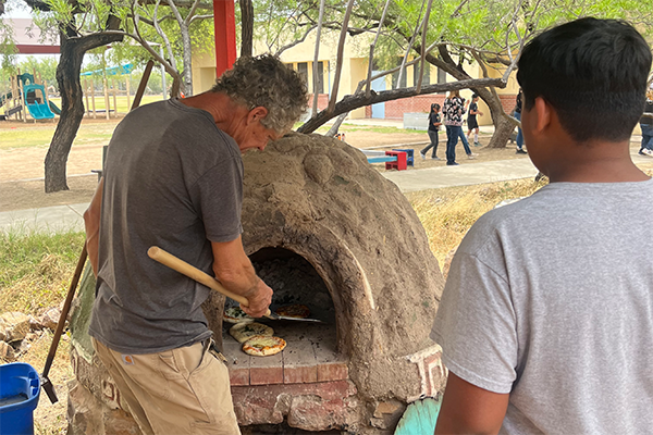 A man puts a pizza into the outdoor oven