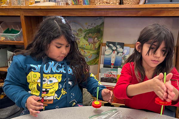 Two girls build spinning tops out of straws