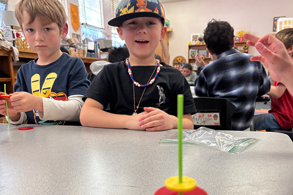 Two boys play with a spinning top made of straws