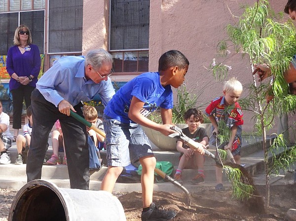 Mayor helping students plant a tree outdoors.