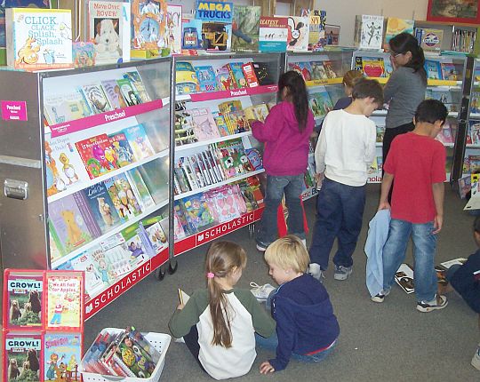 Children at a scholastic book fair viewing books on shelves for sale 